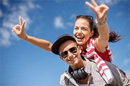 Ilustracja przedstawia dwójkę młodych ludzi: chłopaka w okularach przeciwsłonecznych, który trzyma na swoich plecach uśmiechętą dziewczynę, trzymającą ręce w górze