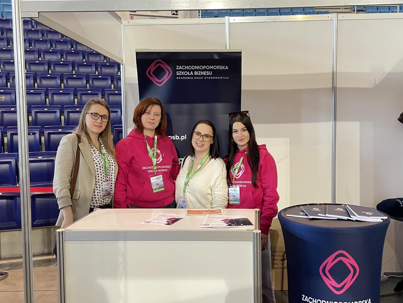 Cztery kobiety pozują na stoisku reklamowym zachodniopomorskiej szkoły biznesu