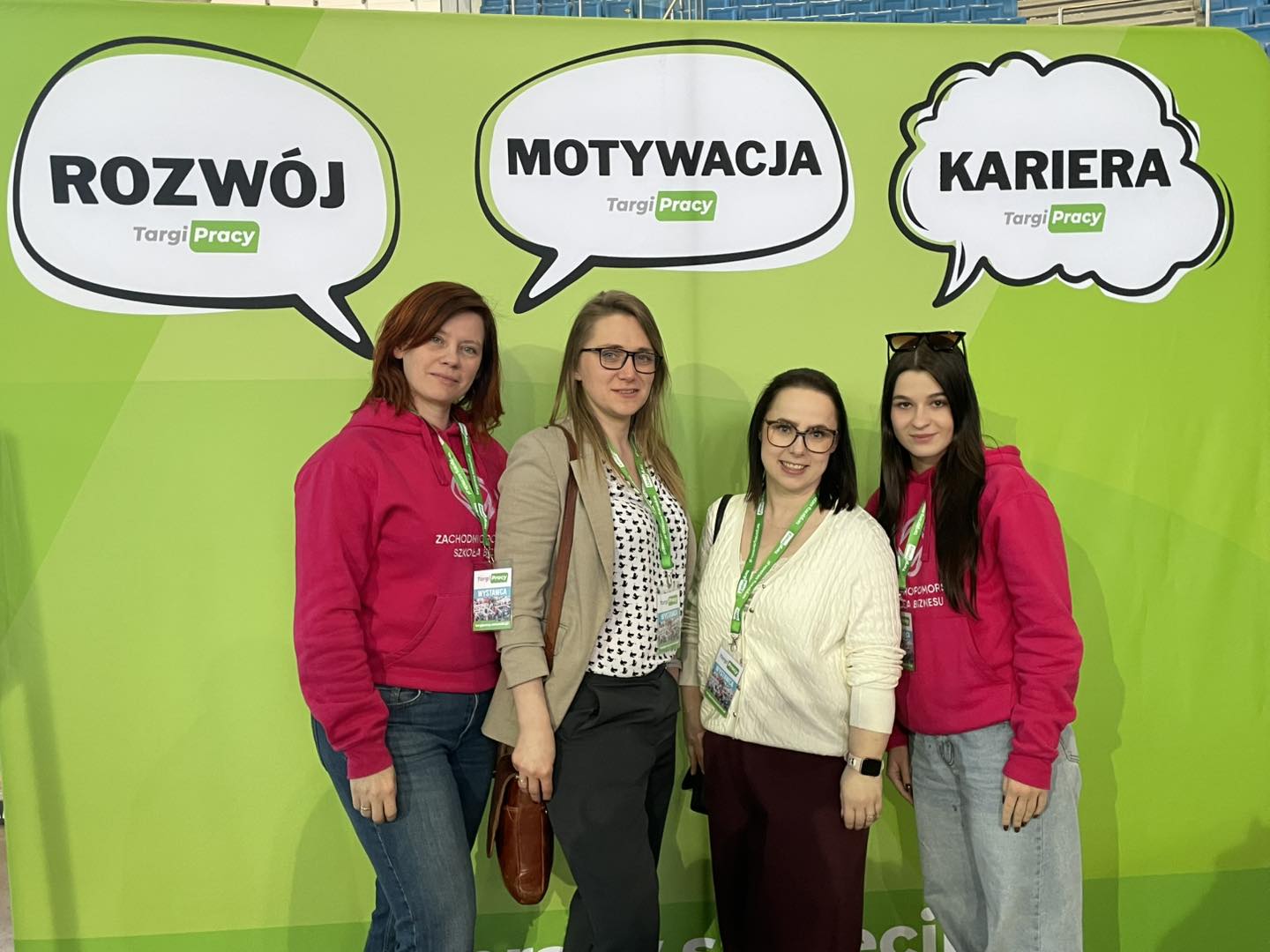 Cztery kobiety pozują na zielonej ściance reklamowej Targów Pracy