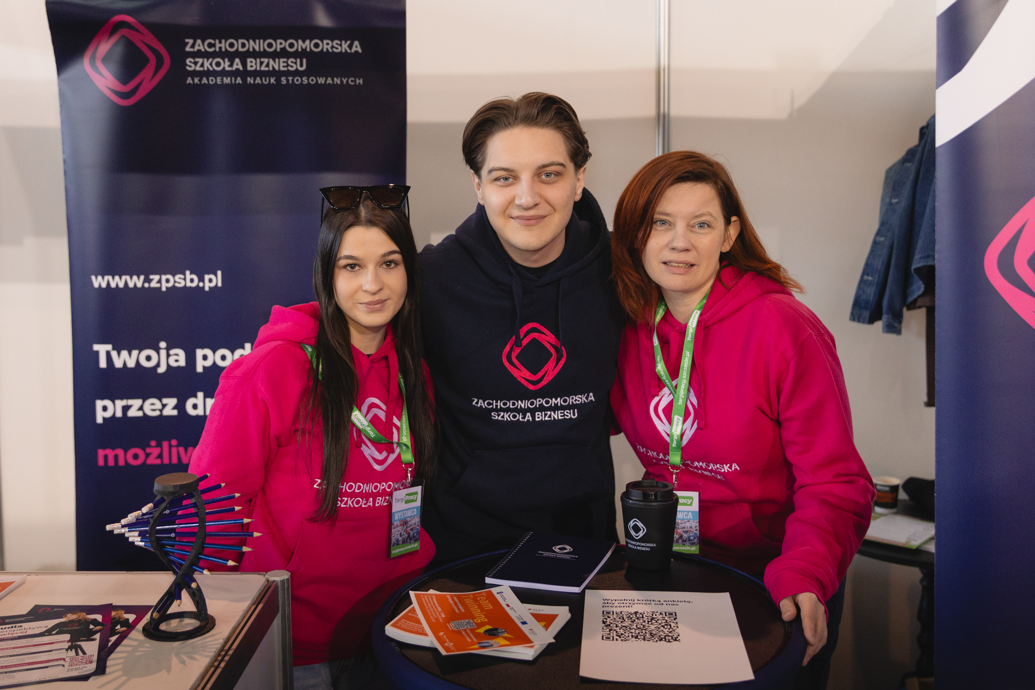 Dwie kobiety i mężczyzna pozują do zdjęcia na stoisku reklamowych Zachodniopomorskiej Szkoły Biznesu