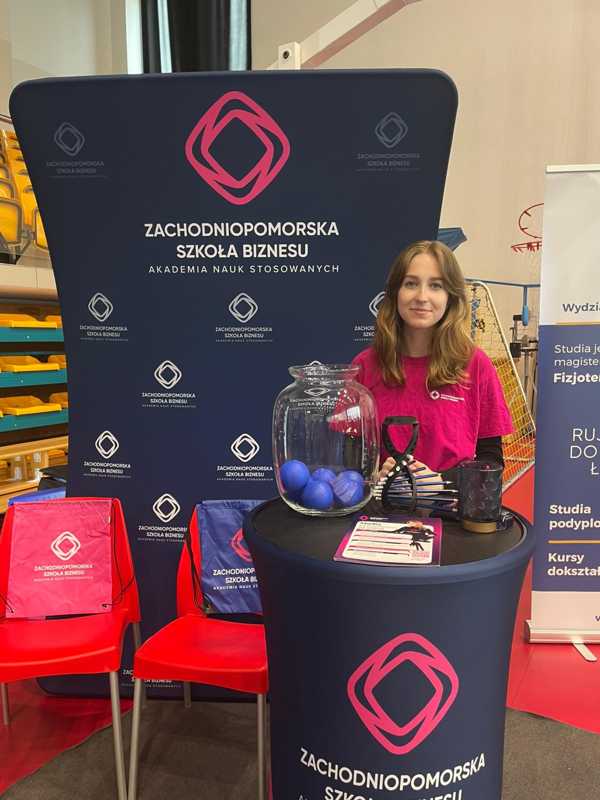 Studentka ZPSB stoi przy stoisku reklamowym uczelni