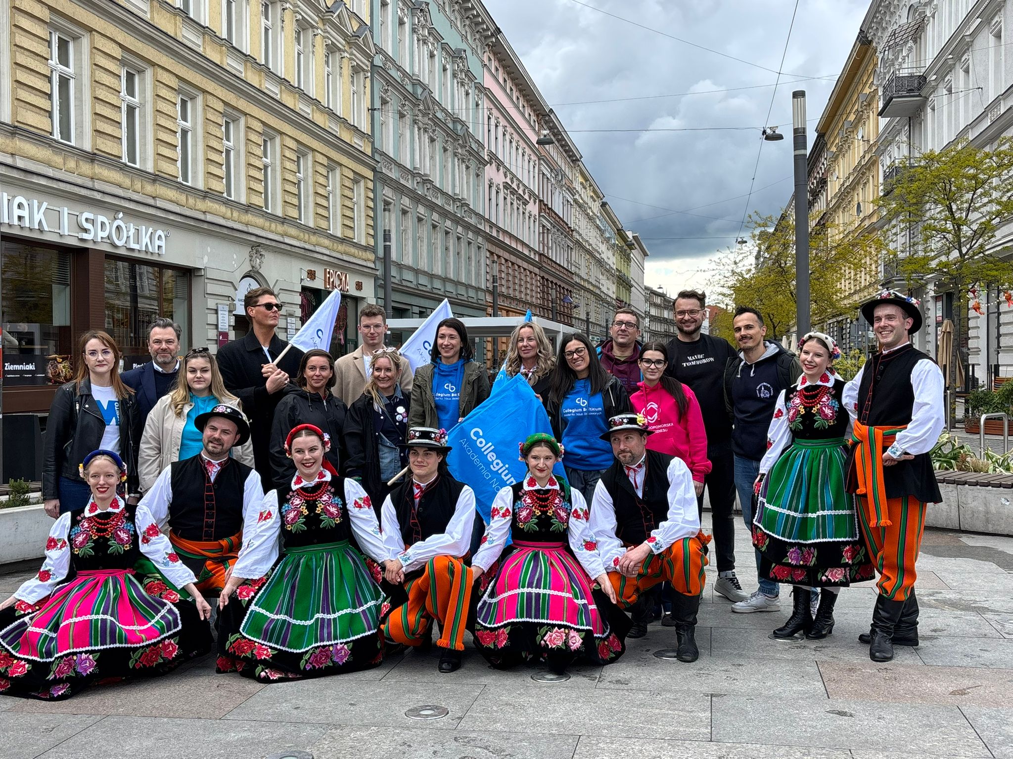 Grupa uczestników Akademickiego Festiwalu Sztuki i Nauki PRZEPŁYW na deptaku w Szczecinie wraz z zespołem folklorystycznym w tradycyjnych strojach ludowych.